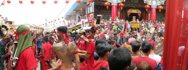 A street in front of a temple and lined with red lanterns is filled with crowds