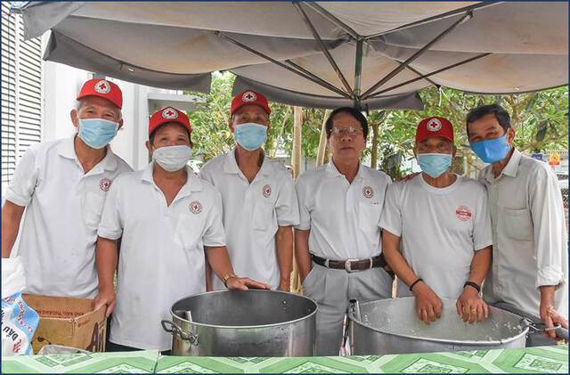 A group of volunteers wearing face masks stand behind large metal cooking pots