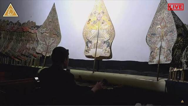 Still image of a Javanese puppeteer in front of the shadow theatre screen. Screenshot from "Doa untuk Dunia" performance of "Sudamala" story by Ki Purbo Asmoro (2020) posted on YouTube.