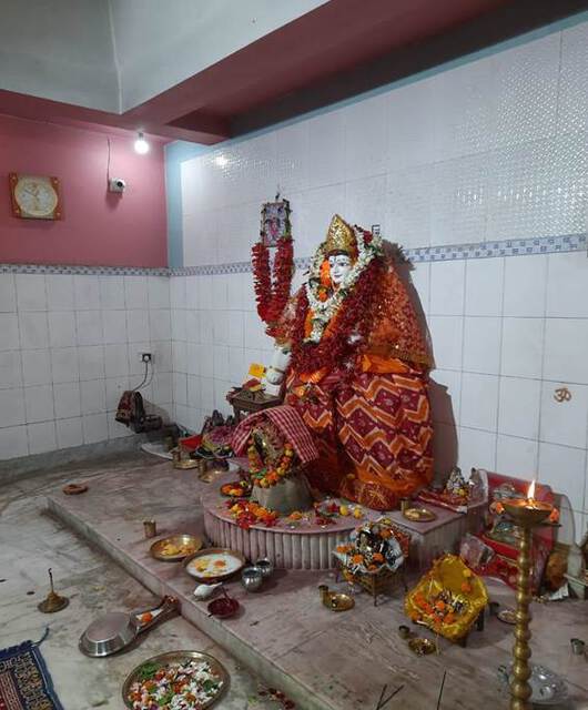 Photo of a statue of a goddess decorated with cloth and flowers inside a temple.