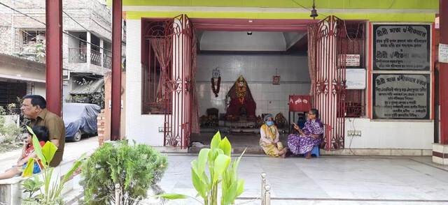 Photo of a temple from outside with ist doors open and four people sitting in front of it.