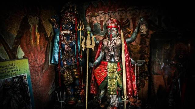 Close up photo of a statue of Bhadrakali, a form of Kali, wearing red and gold clothing, with a long red tongue outstretched.