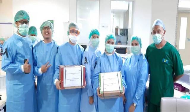 A group of people in scrubs and face masks hold up packaged boxes
