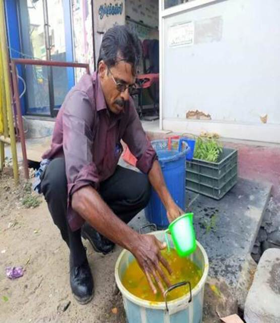 Photo of a man washing with turmeric and neem infused water from a plastic bucket.