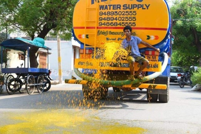 Photo of man sitting on a driving truck spraying the streets with turmeric water.