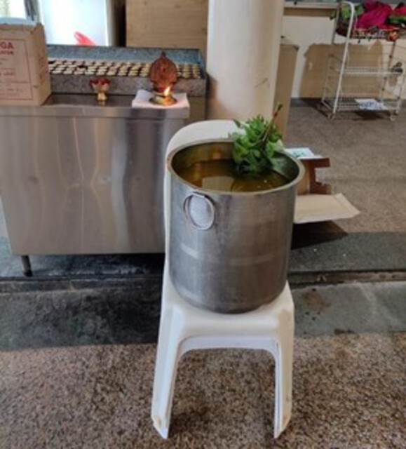 Photo of a pot with turmeric water and neem leaves on a plastic chair.