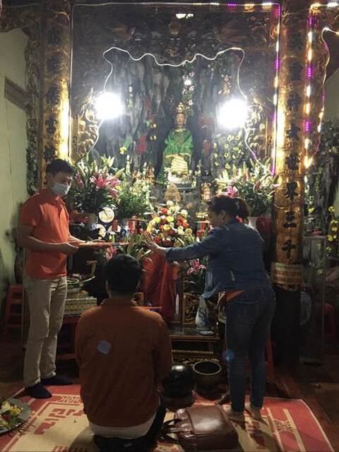 Three worshippers at a Dao Mau altar. Two are standing, one is kneeling. All are wearing masks.
